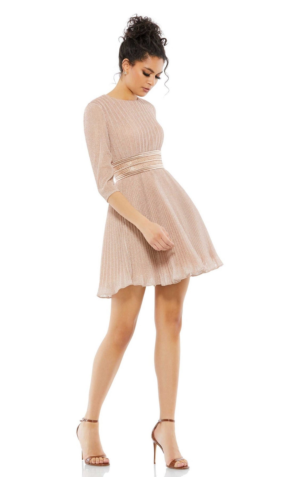 A woman wears the Short Party Dress 30749 by Mac Duggal—a light pink, pleated A-line party dress with long sleeves and a banded waist—paired with strappy high-heeled sandals.